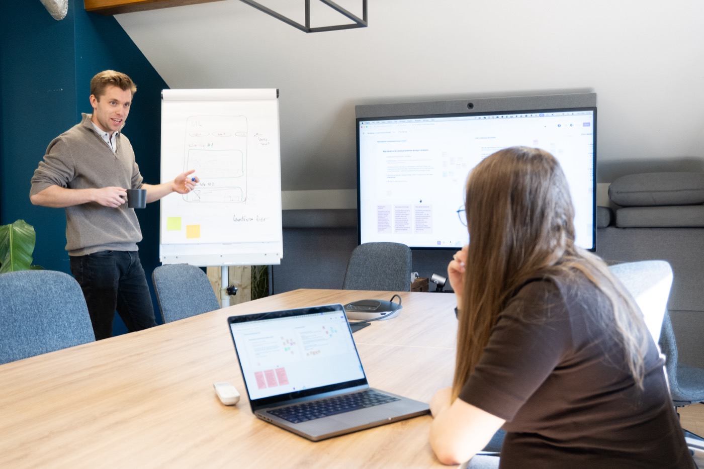 Strategiworkshop: et teammedlem presenterer ved en flipover mens en kollega lytter ved møtebordet
